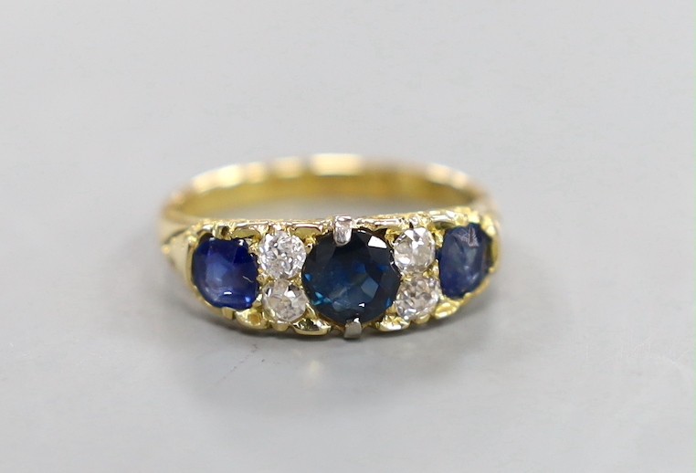 A late Victorian 18ct gold, three stone sapphire, and four stone diamond set half hoop ring, with carved setting, size O, gross weight 4.3 grams.